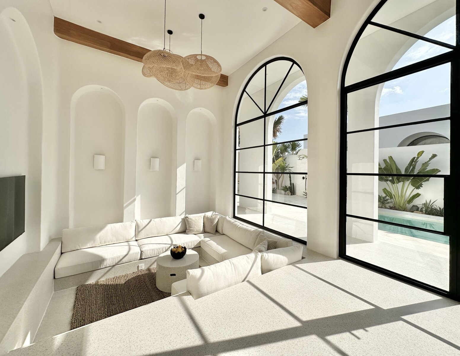 Bright minimalist interior with large arched windows, modern decor, and tropical views.