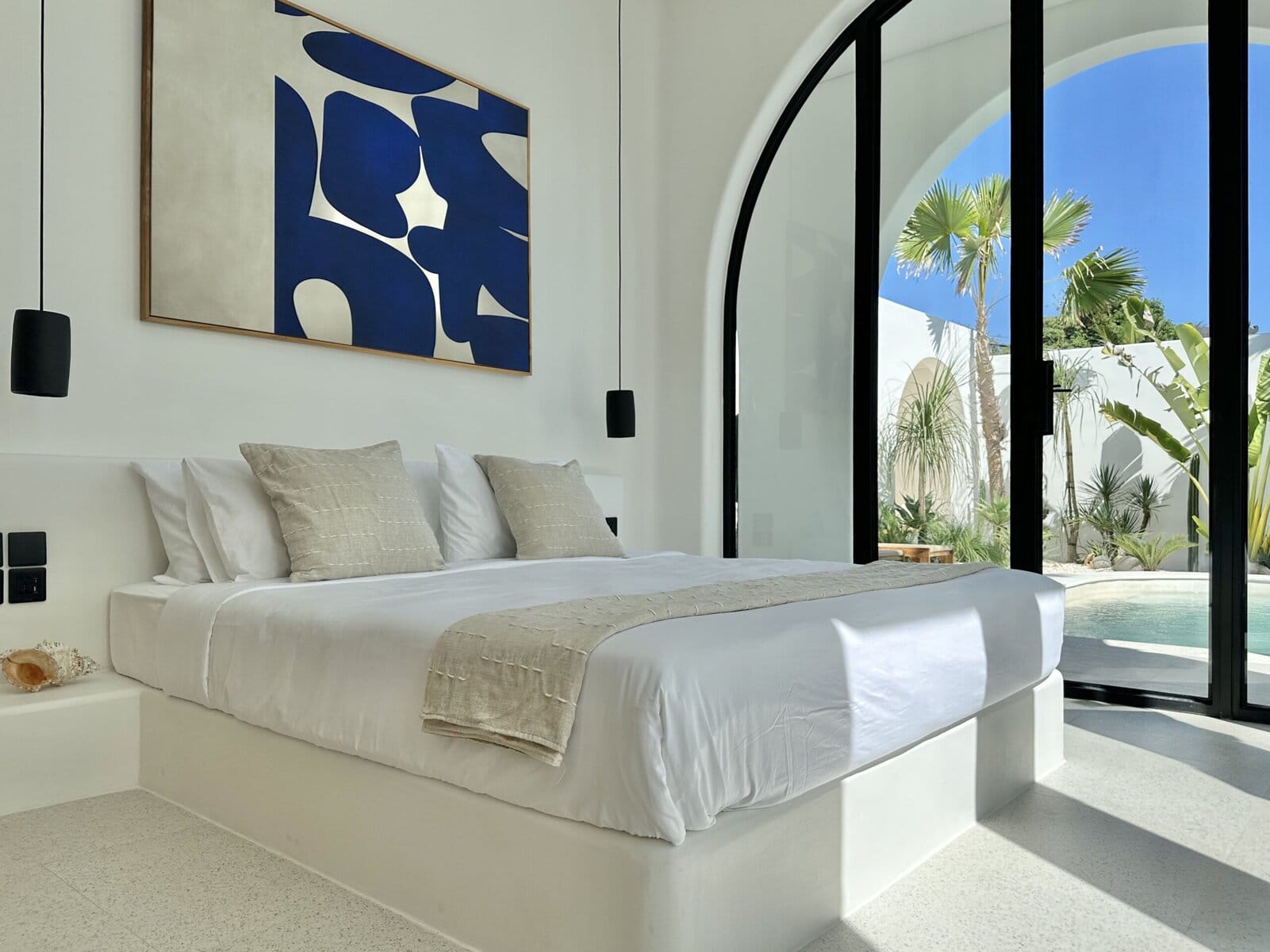 Bright, modern bedroom with minimalist decor, large glass doors, and outdoor pool scene.