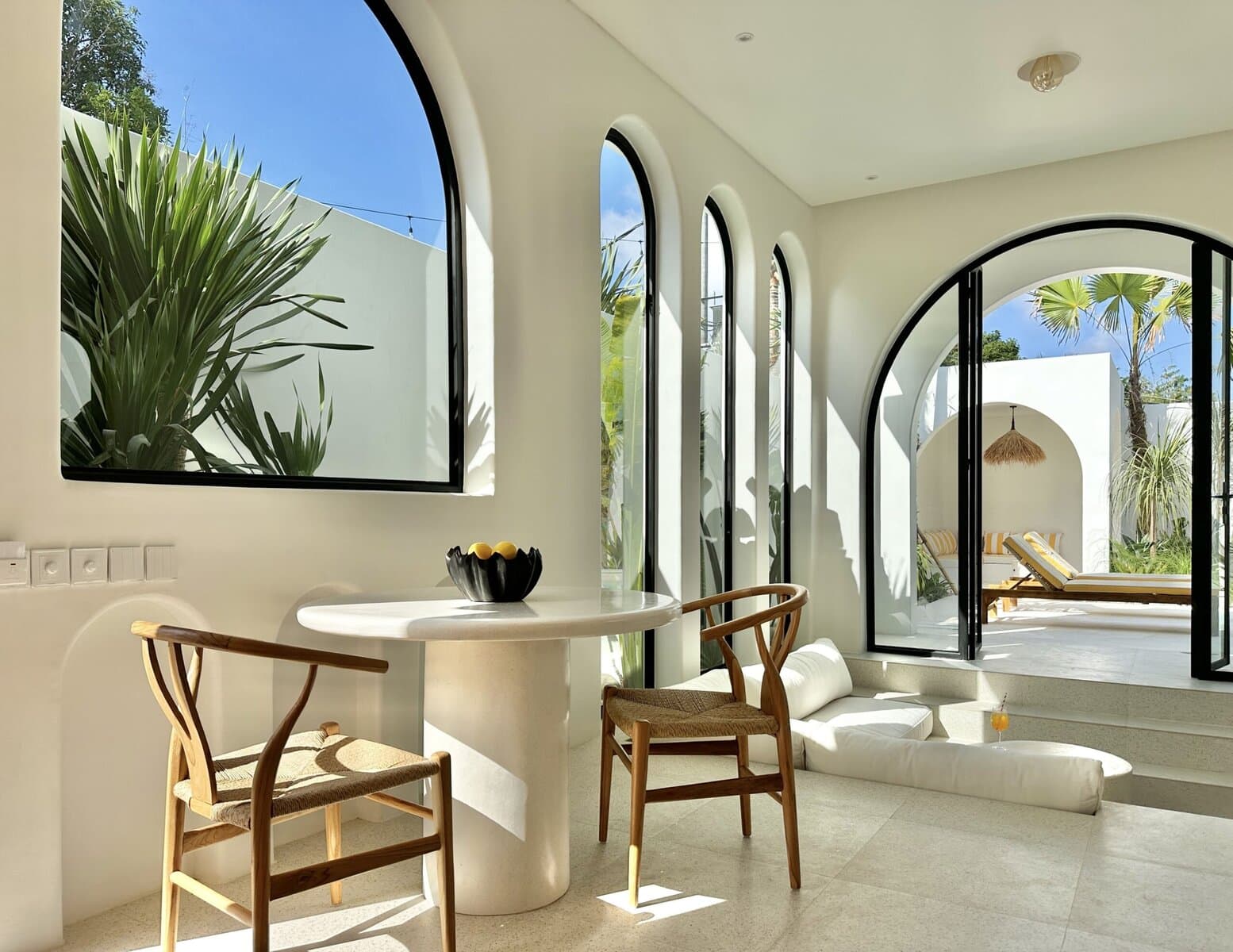 Bright, airy space with large arched windows, lush greenery outside, and tropical decor.