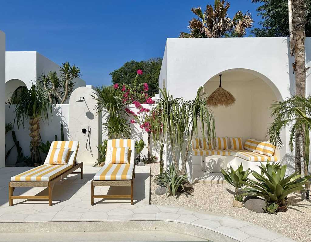 Bright, minimalist white villa with sun loungers and tropical decor.