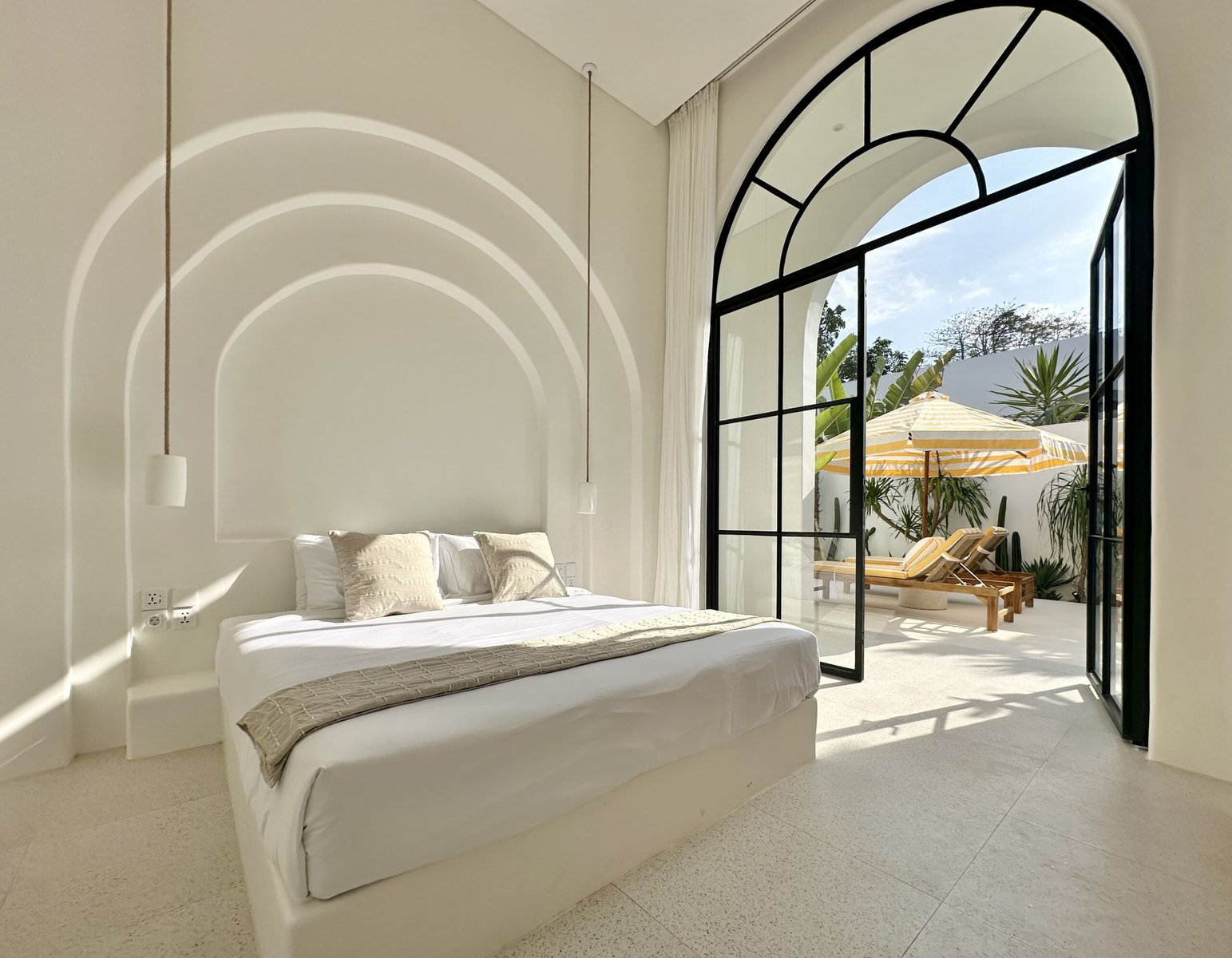 Spacious bedroom in Bali with large glass doors opening to outdoor tropical lounge area.