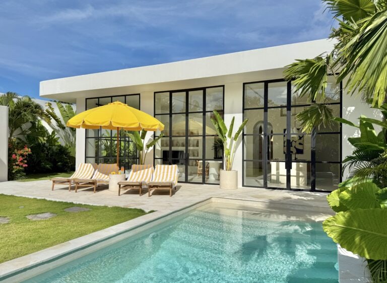 Bright, open-concept villa featuring floor-to-ceiling glass walls and lush tropical landscaping.