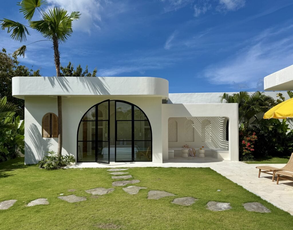 Stylish white exterior with modern curves, lush greenery, and tropical plants.