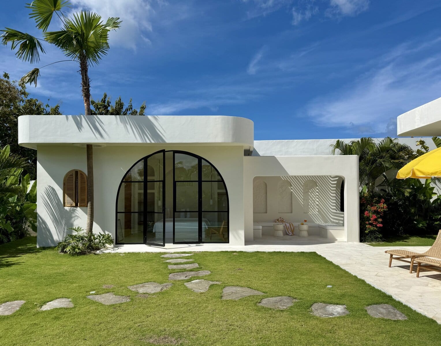 Stylish white exterior with modern curves, lush greenery, and tropical plants.