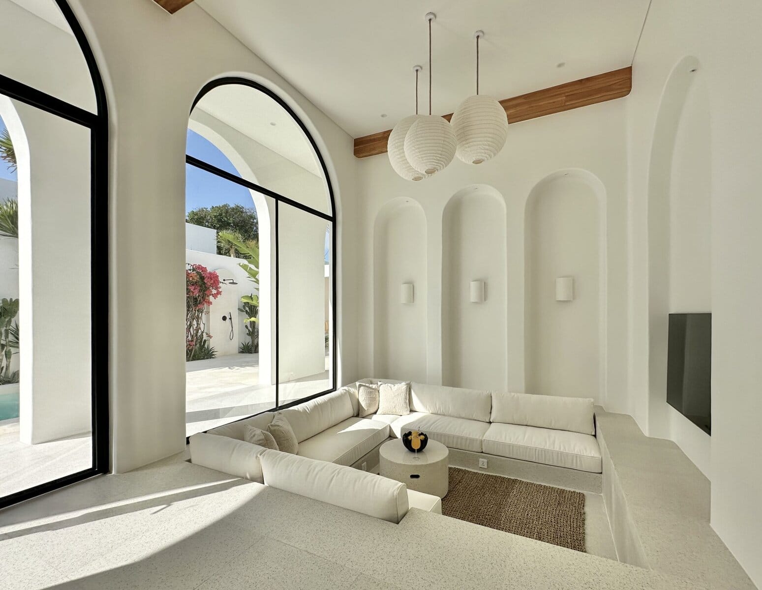 Bright and modern Bali villa living space with large arched windows and neutral color palette.