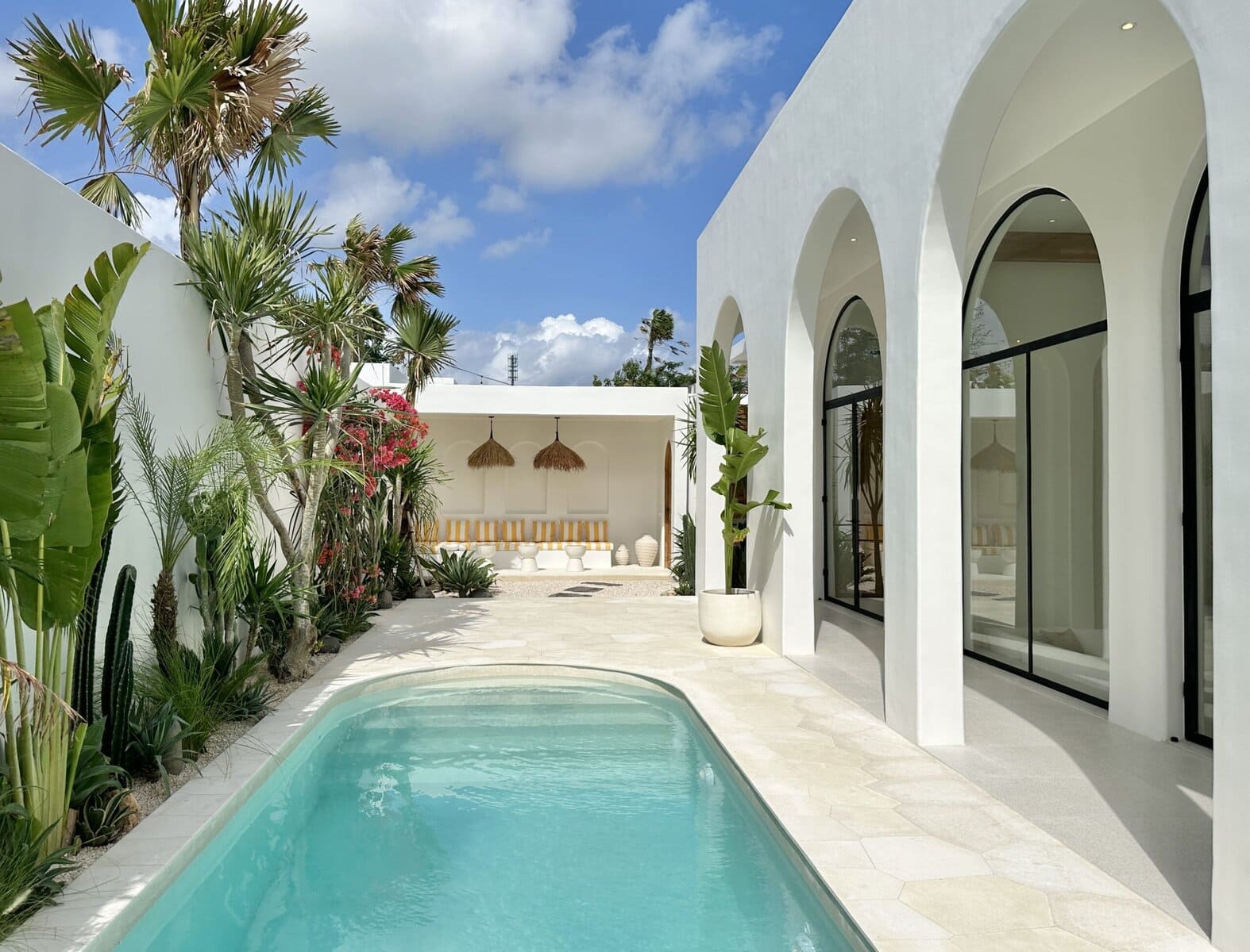 Modern tropical villa in Uluwatu with pool, white arches, lush greenery, perfect for vacation stays.