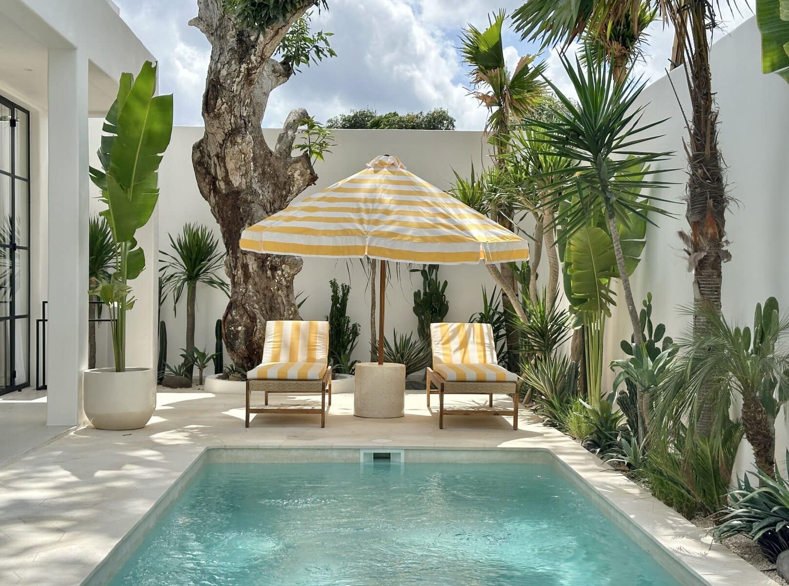 Beautiful outdoor space featuring a pool, sun loungers, and lush greenery with shaded seating.