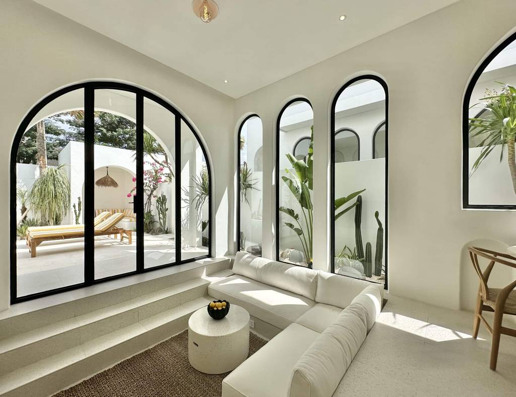 Bright modern living room with large arched windows and lush greenery view.