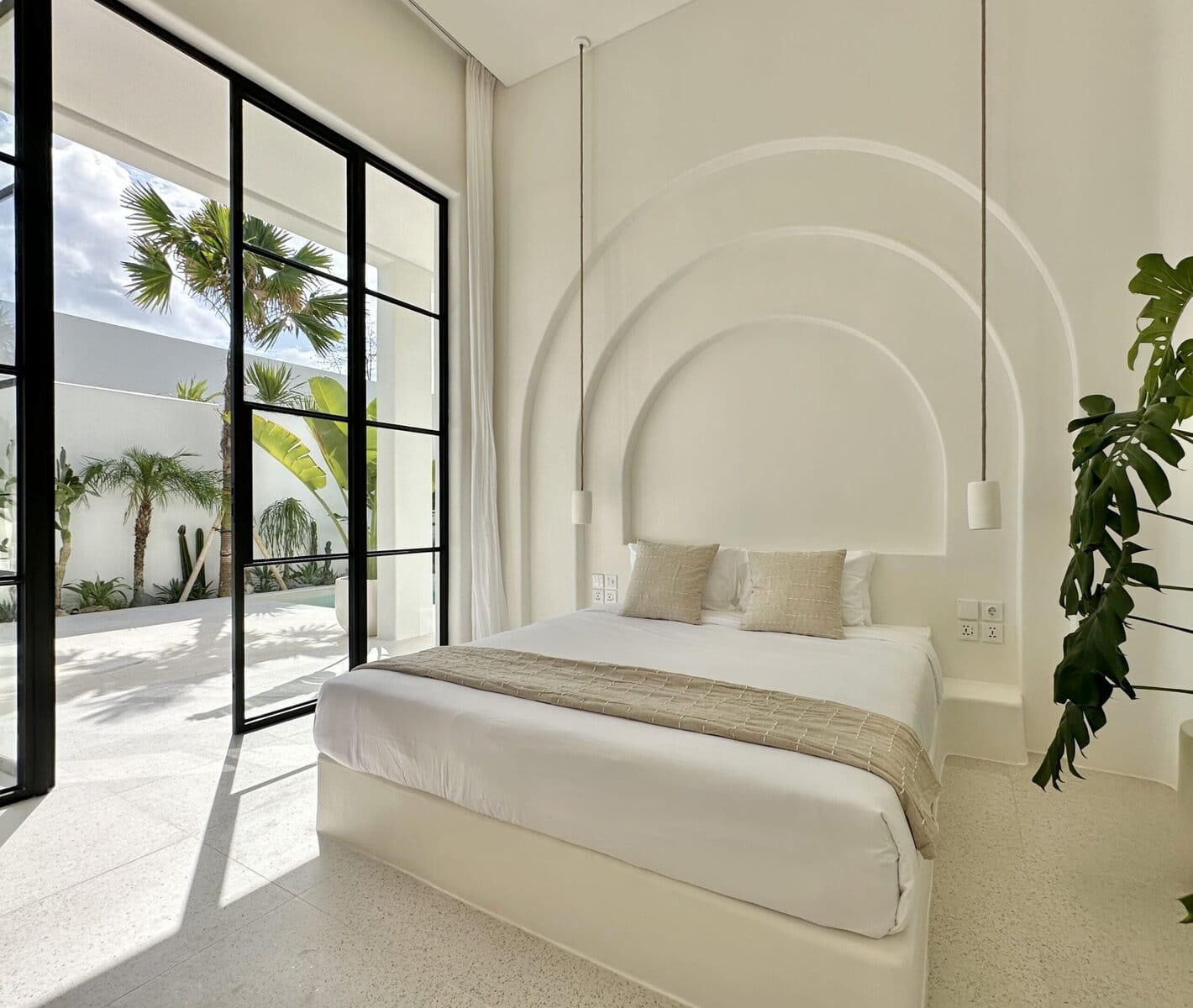 Bright minimalist bedroom with spacious glass doors opening to tropical outdoor space.