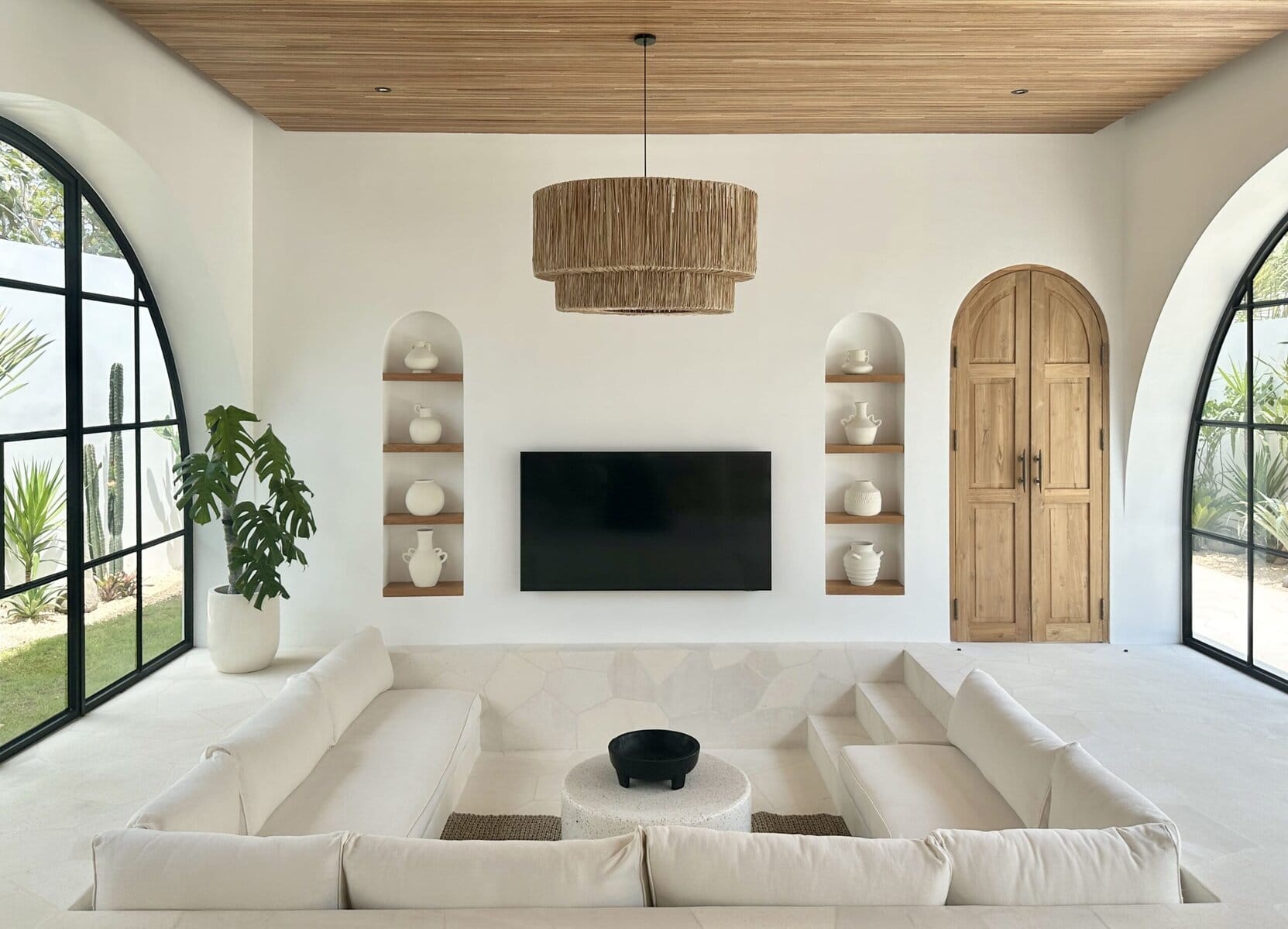 Elegant living room with large arched windows, white furnishings, and stylish shelving featuring white ceramics.