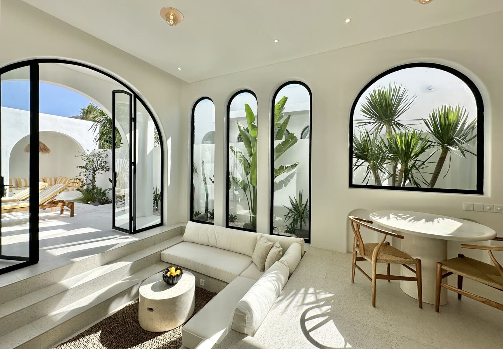 Stunning indoor view of a Bali vacation villa with large arched windows and lush greenery outside.