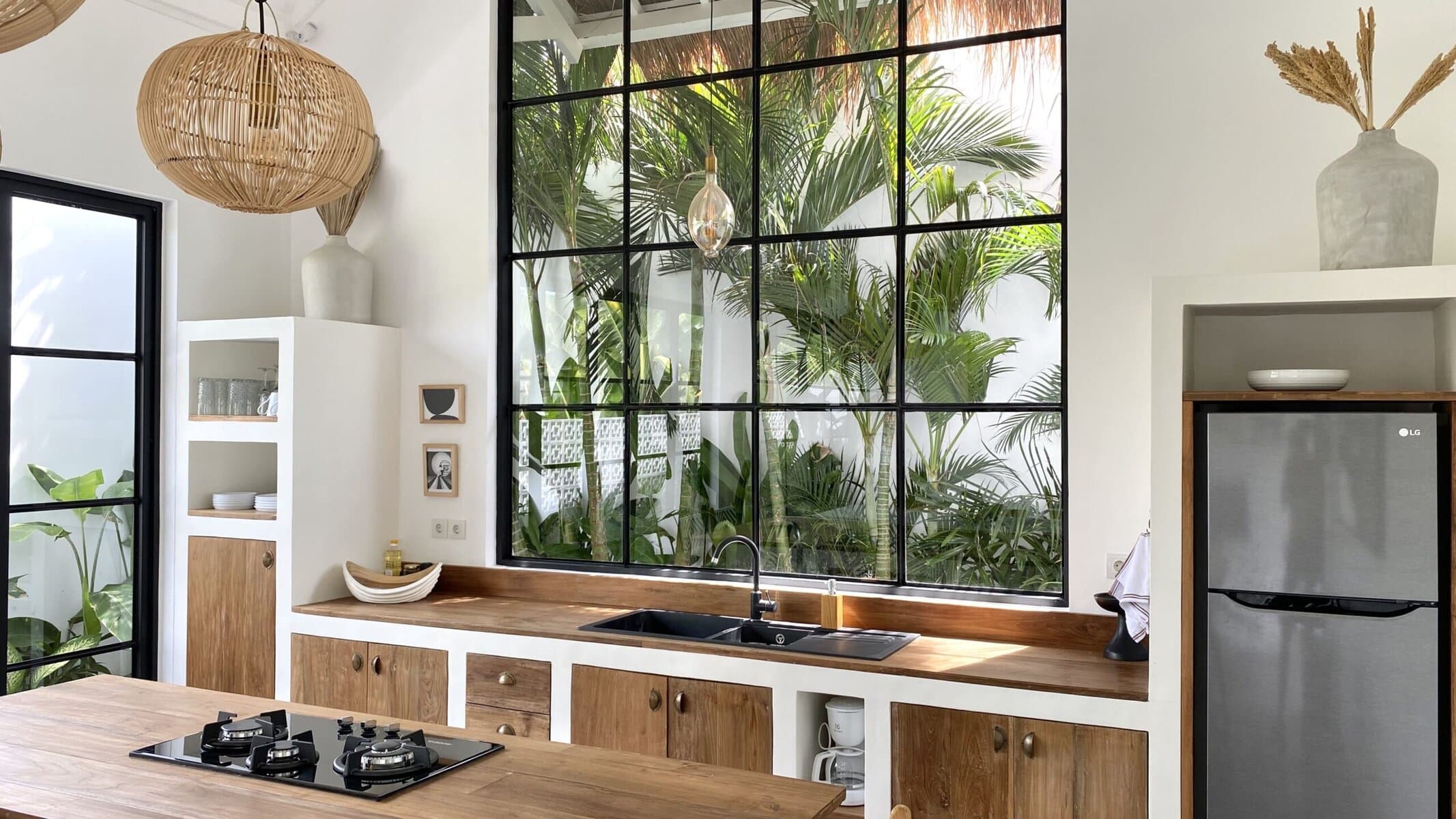 Bright, modern kitchen with natural wood accents and large glass windows showcasing lush tropical surroundings.