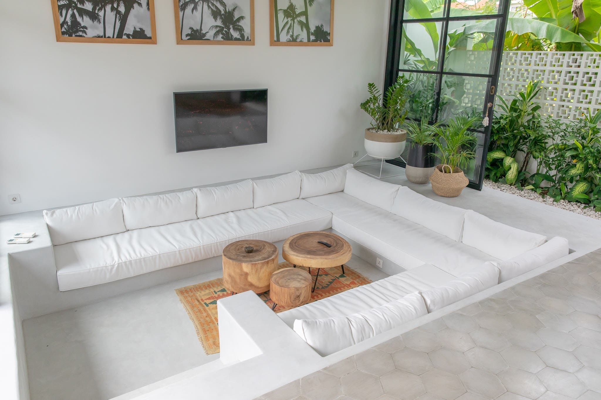 Modern minimalist living room with white sofa, wooden tables, and lush greenery outside. Perfect for a luxury Bali getaway.