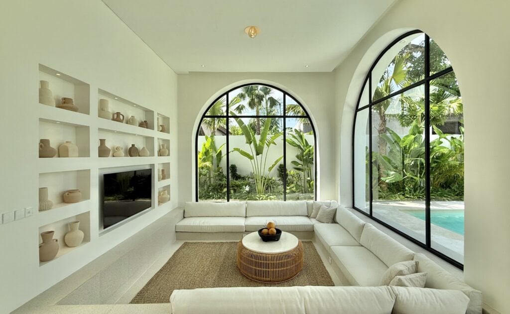 Bright modern living room with large arched windows and lush garden view in Bali.