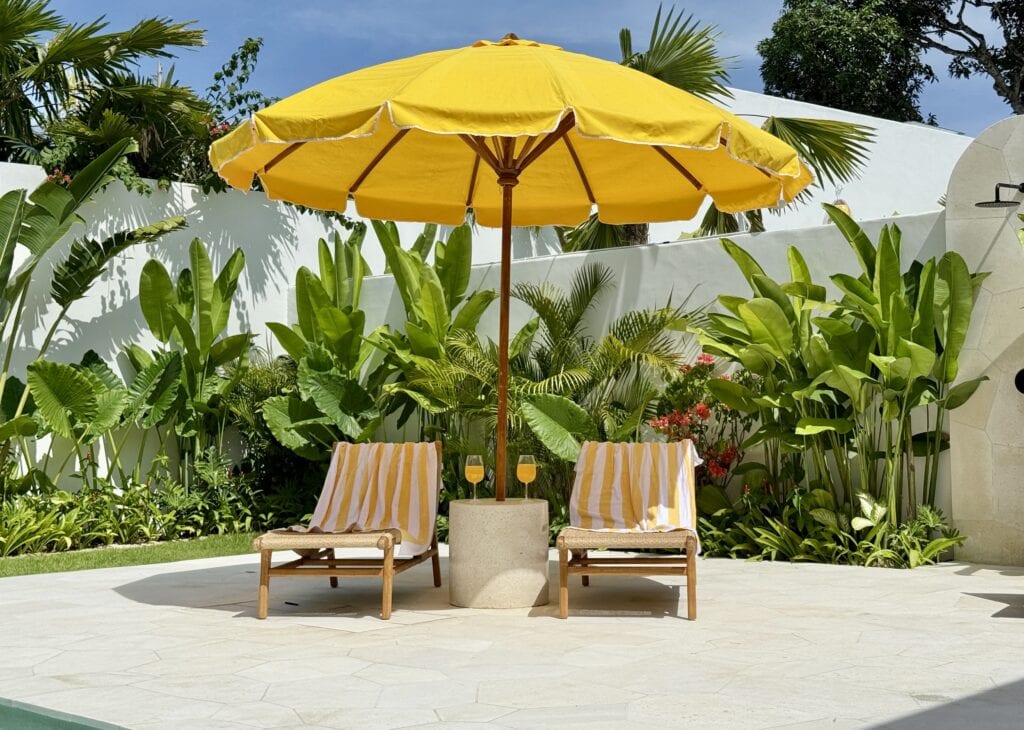High-end modern outdoor seating with yellow umbrella, surrounded by lush tropical plants.