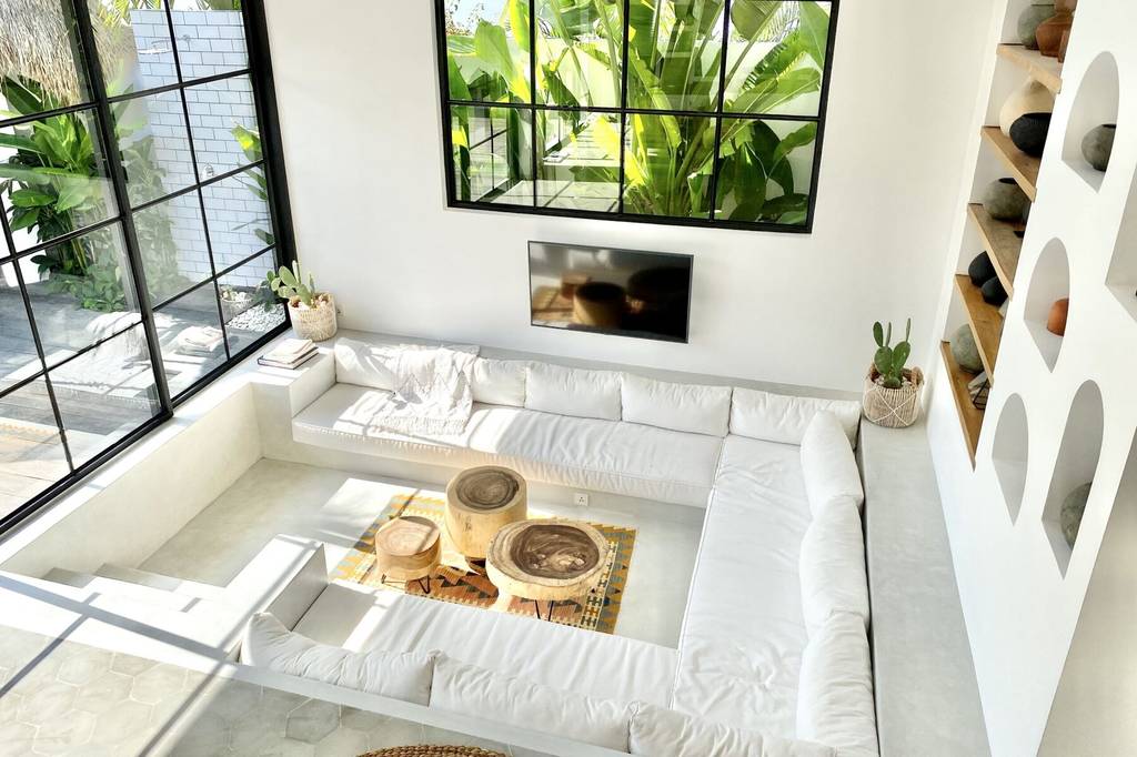 Bright living room featuring white seating, large windows, and greenery for a tropical vibe.