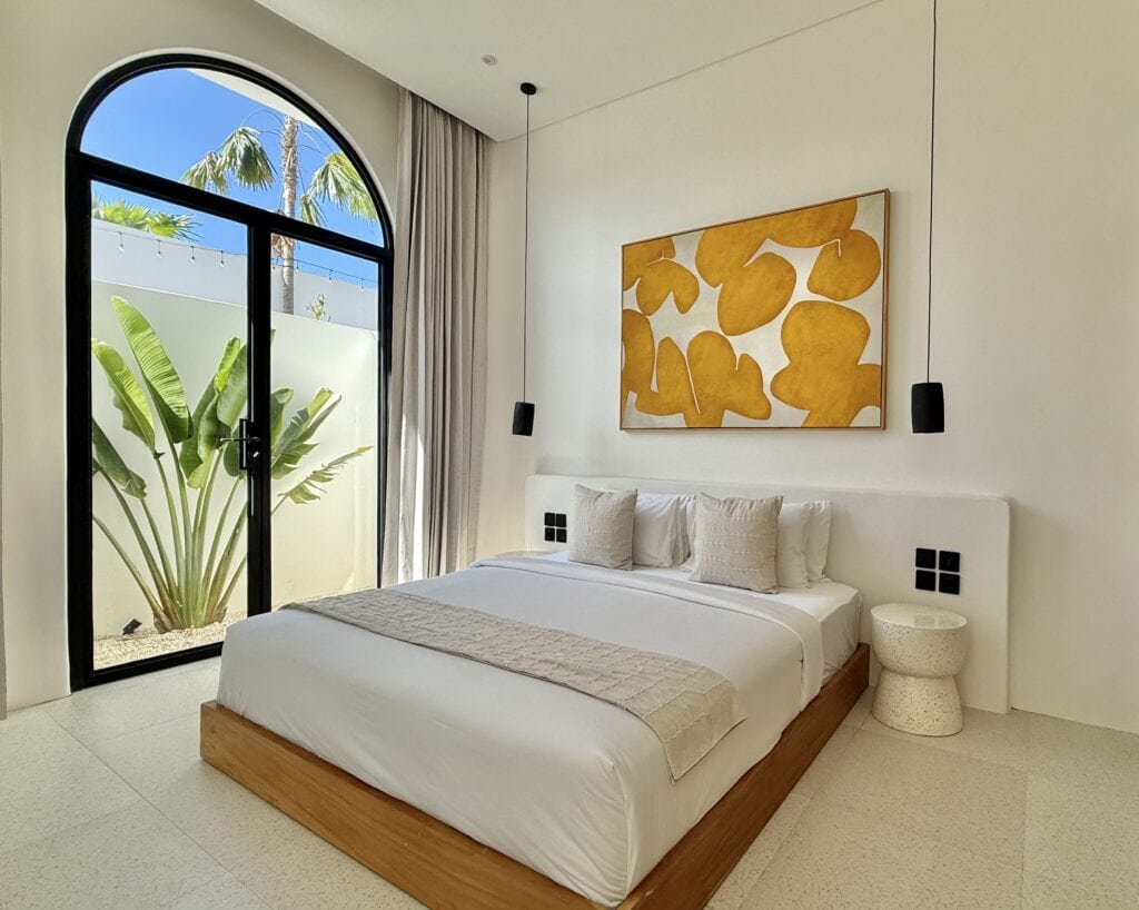 Stylish tropical-modern bedroom with minimal decor and large glass doors opening to tropical outdoor views.