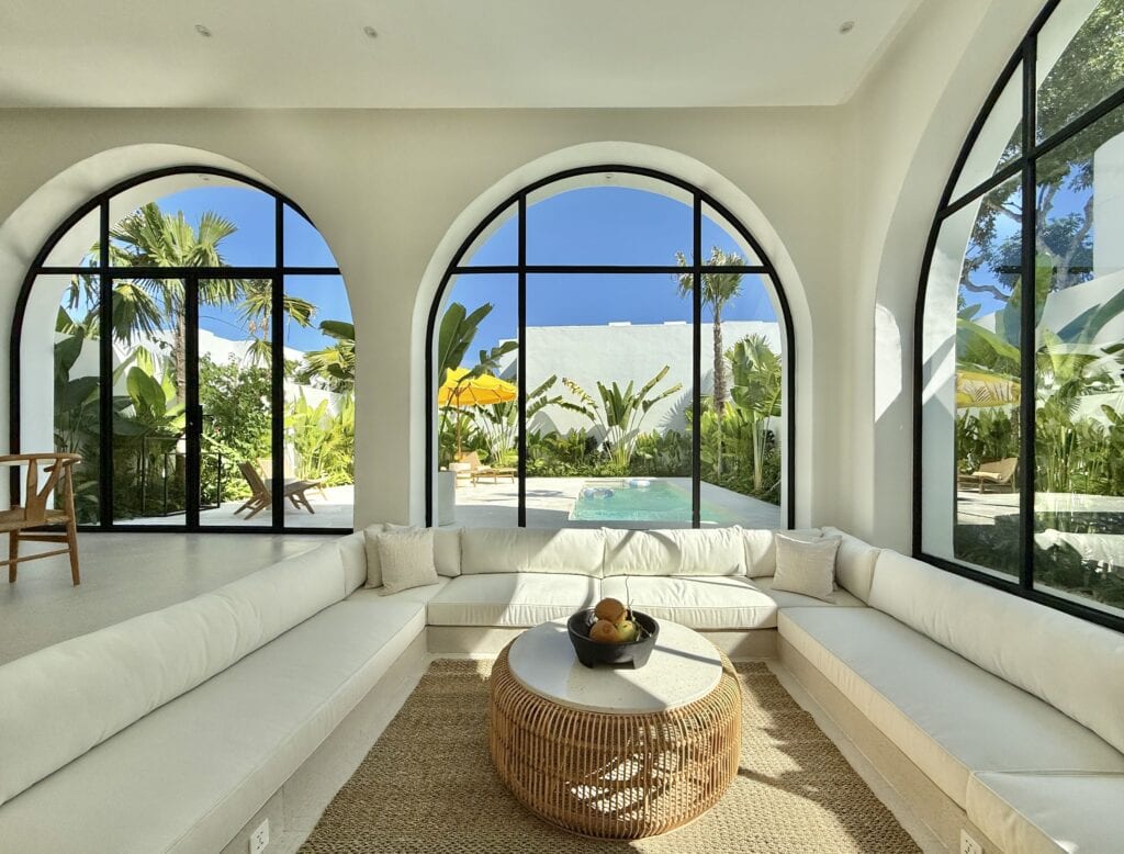 Bright, airy living space with large arched windows overlooking lush garden and pool in Uluwatu.