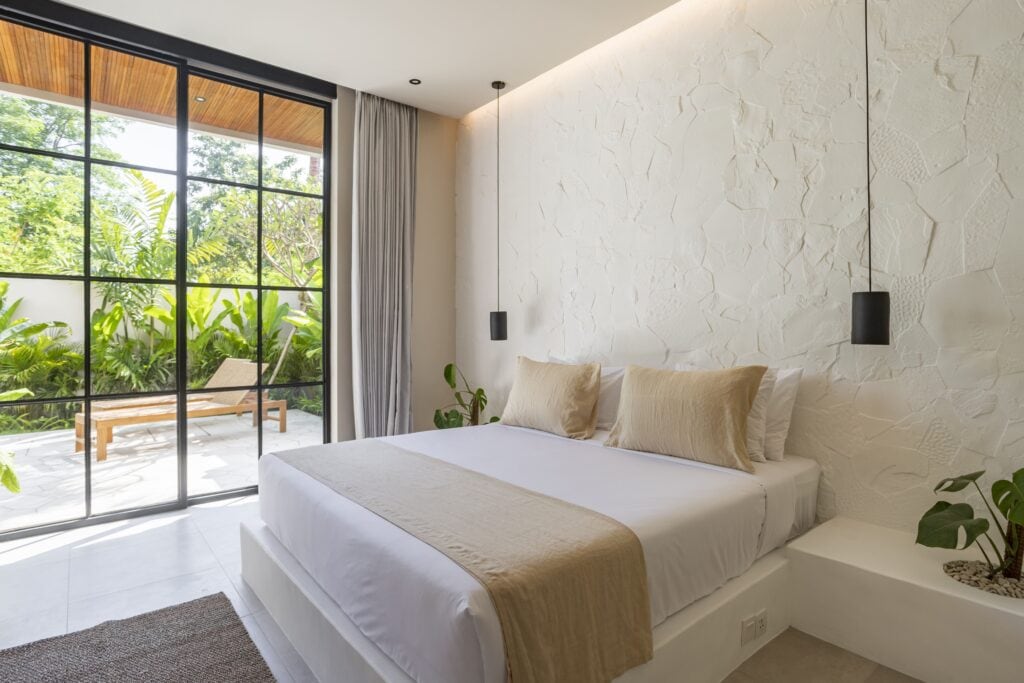 Modern tropical bedroom with balcony and lush greenery outside.