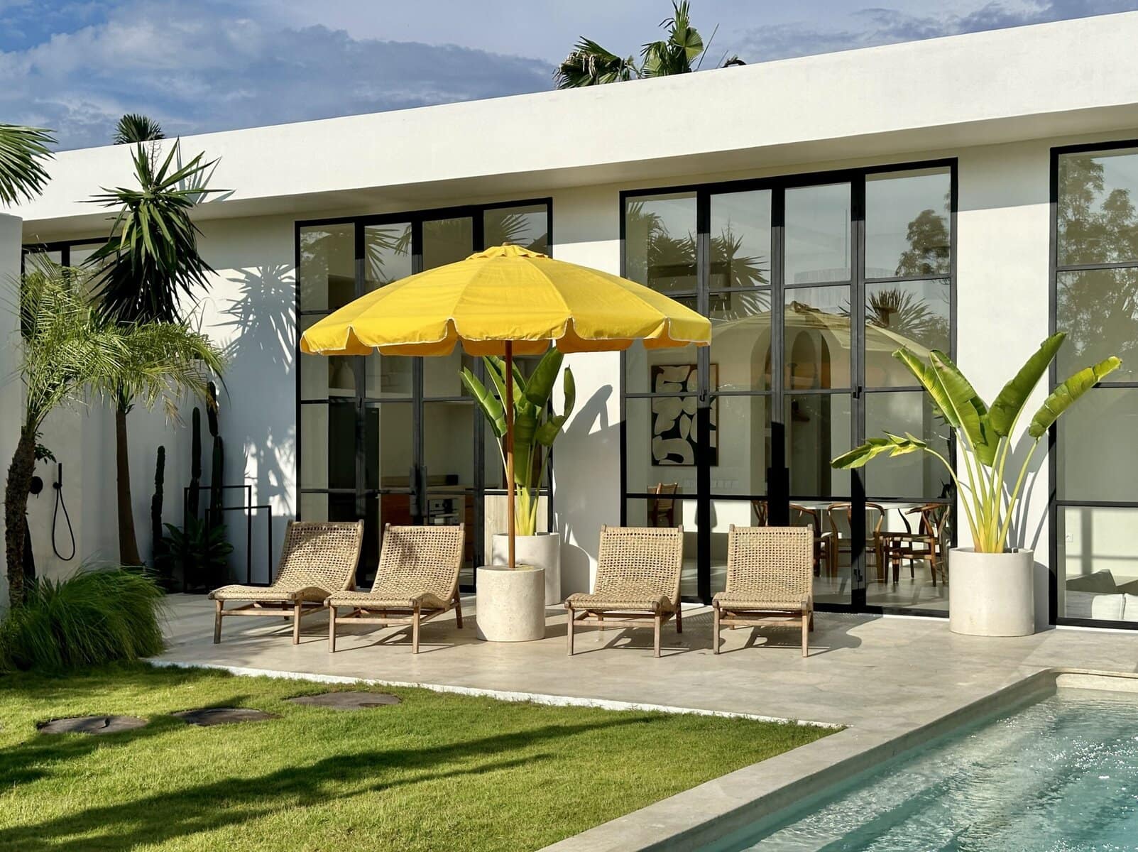 A modern villa in Uluwatu with sleek design, poolside loungers, lush plants, and a vibrant yellow umbrella.