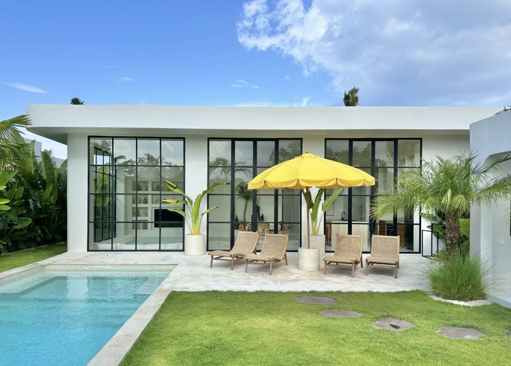 Stepping outside this modern villa in Uluwatu, enjoy a private pool, sun loungers, and tropical plants, ideal for relaxing or entertaining in style.