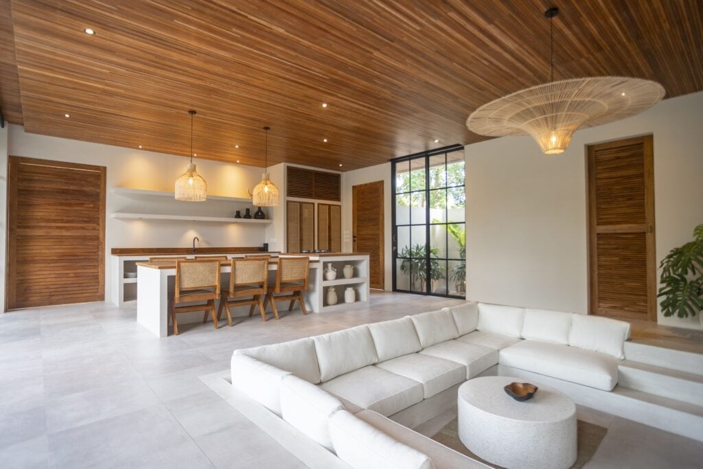 Modern tropical living space with wooden accents, spacious white sofa, and open kitchen design.