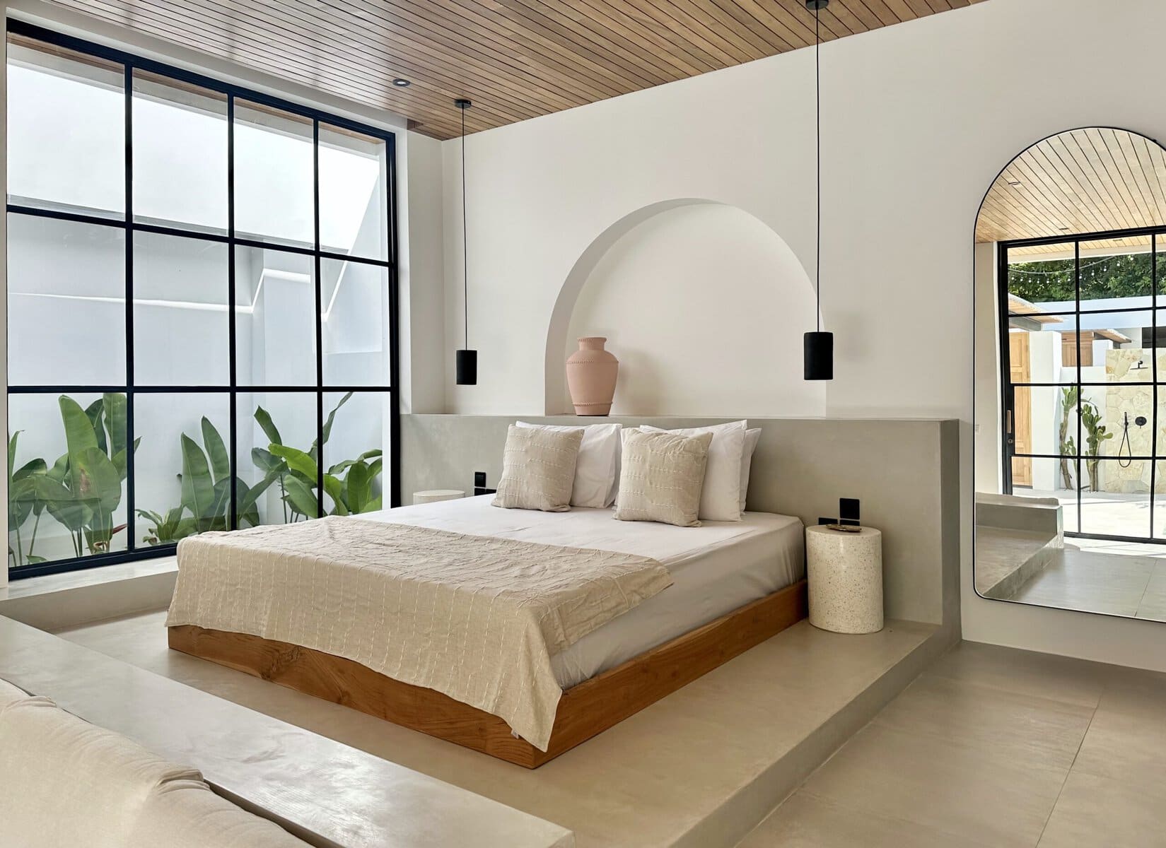 Elegant bedroom featuring neutral tones, large window with tropical garden view, and contemporary decor.