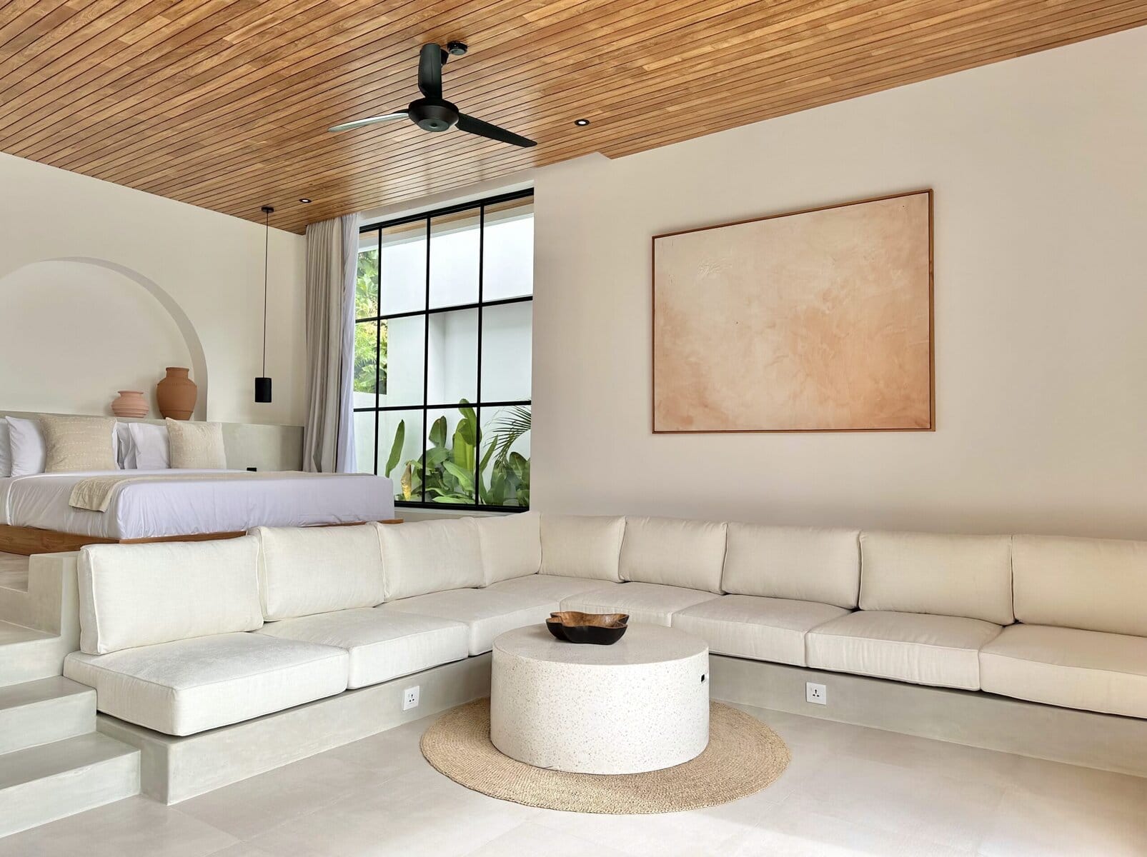 Bright, minimalist interior with a cozy lounge and bedroom view, blending modern comfort with tropical elegance.