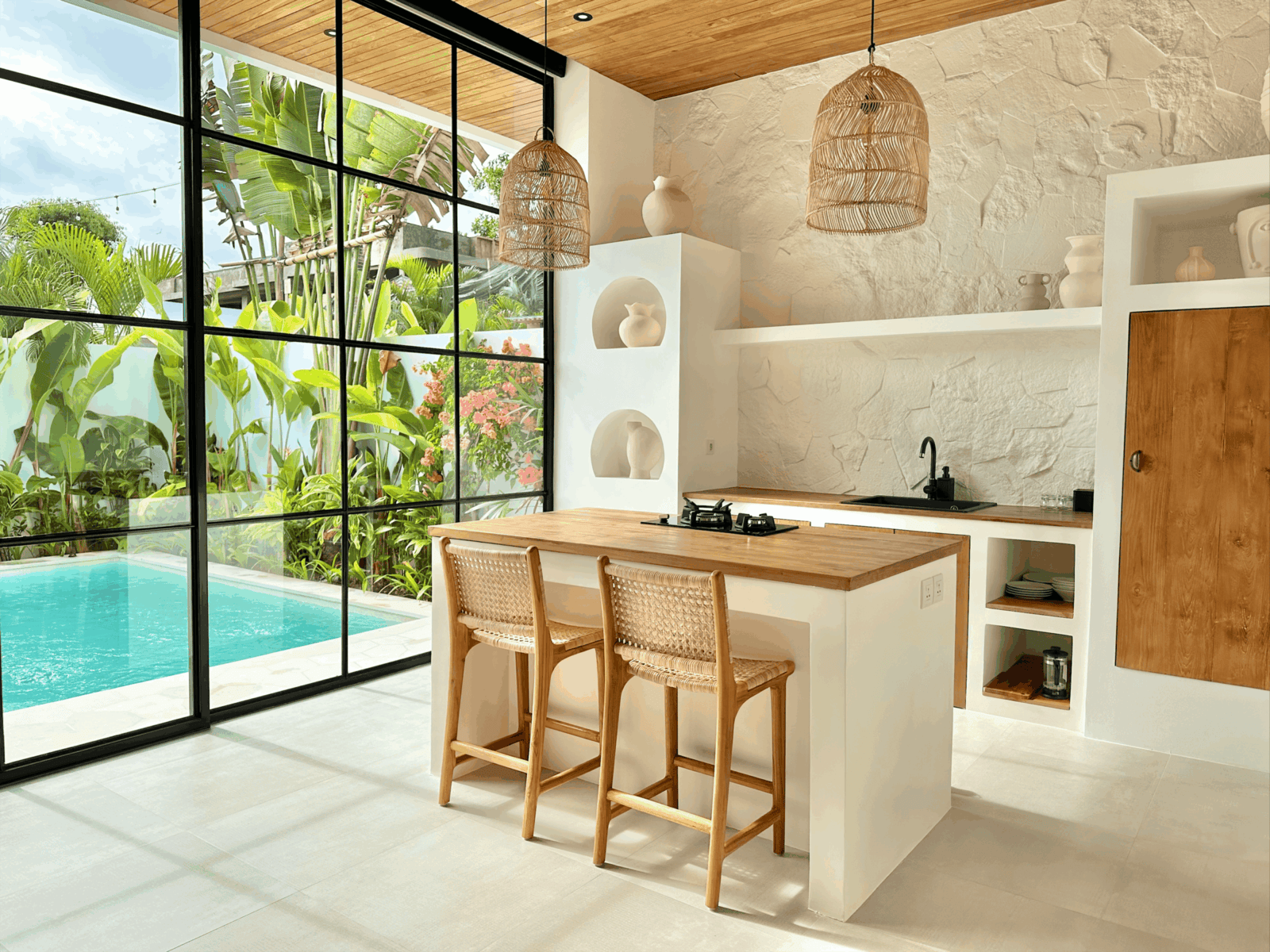 A minimalist Bali villa featuring an open kitchen, large glass windows, and private pool in a serene Uluwatu setting.