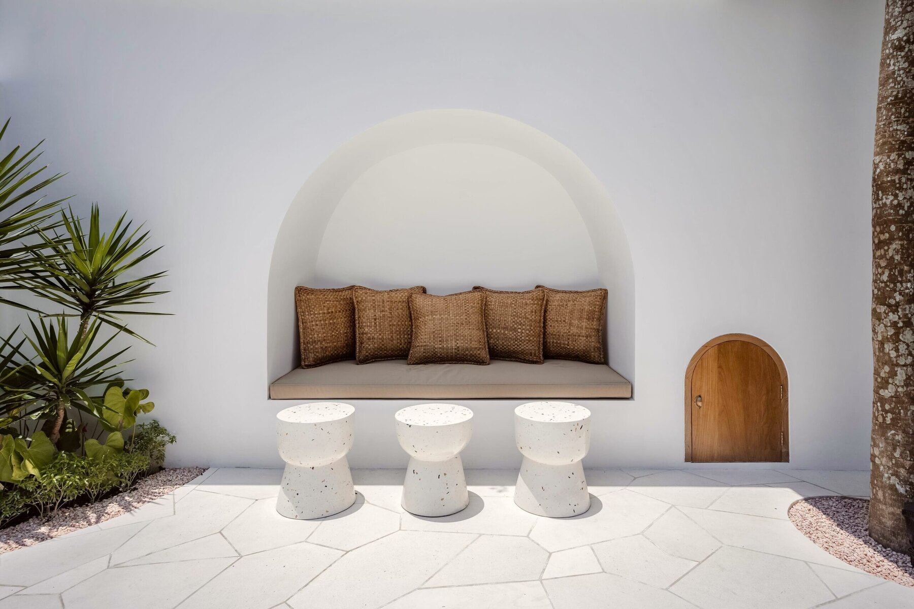 Stylish minimalist outdoor lounge with white walls, rattan cushions, and modern terrazzo stools.