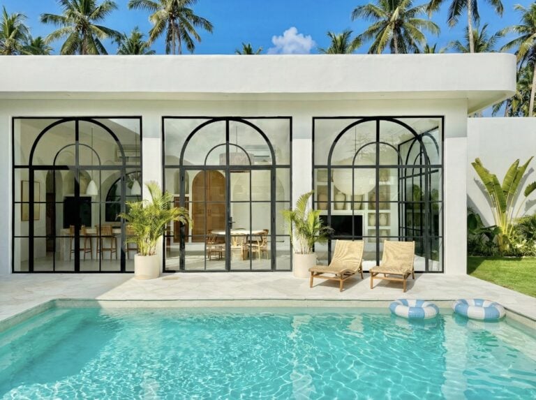Modern tropical villa with glass doors, pool, and lush greenery in Uluwatu, Bali.
