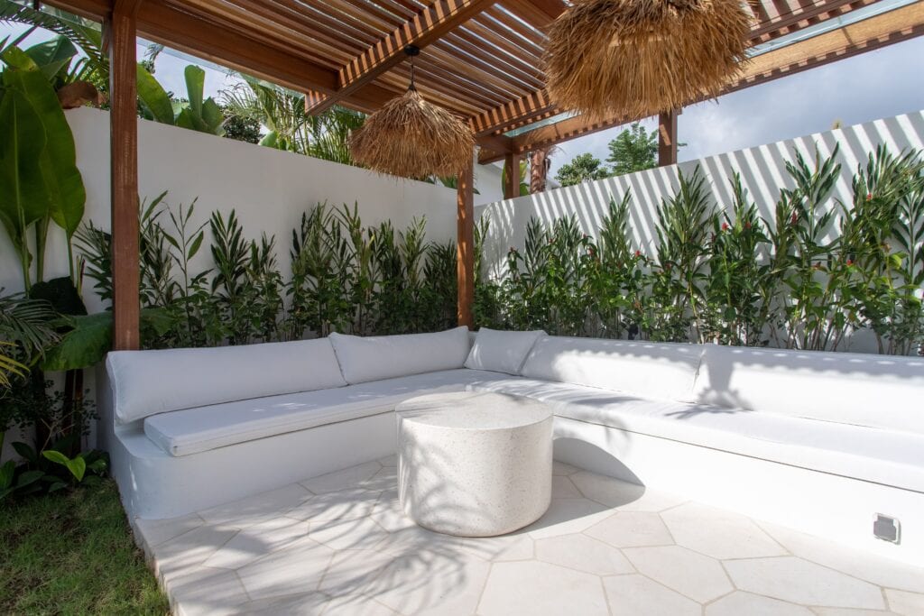 Elegant white outdoor sofa with tropical plants and shaded pergola outdoors.