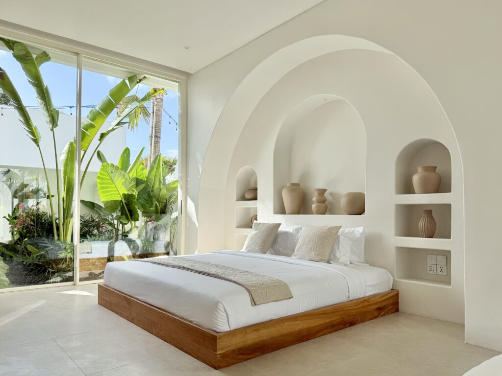 Bright, airy bedroom with tropical garden view, minimalist design, high-end finishes, and natural light.