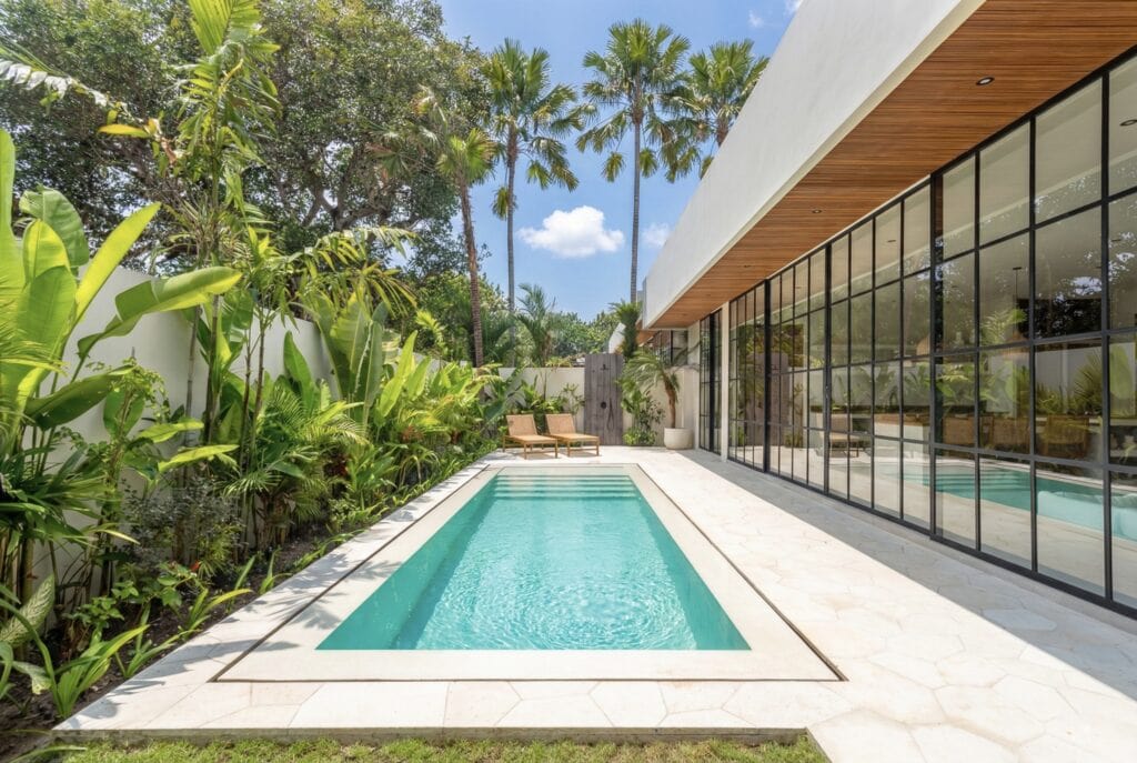 Modern tropical villa with private pool and lush greenery in Bali. High-end design, glass walls, and sophisticated decor.